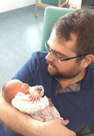 Richard Cox segurando sua filha recém-nascida