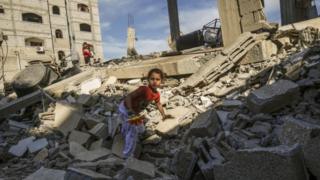 Uma menina palestina sobe nos destroços de um prédio que foi destruído por um ataque israelense em 5 de maio