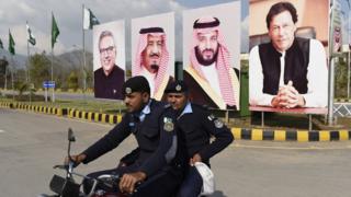 Policemen in front of large posters of Imran Khan and MBS
