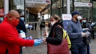 Volunteers distribute face masks and leaflets to commuters in front of the Gare du Nord train station in Paris on April 29, 2020,