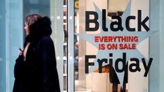 Shoppers pass a promotional sign for 'Black Friday' sales discounts, outside a store on Oxford Street in London, on November 26, 2019