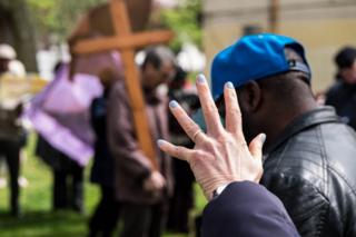 A woman holds a hand up to a cross that is being carried
