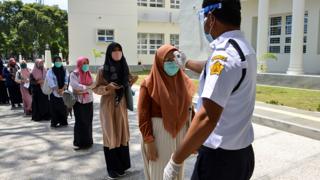 A security guard wearing a face shield checks a student's temperature at a university in Banda Aceh, Indonesia - 5 July 2020