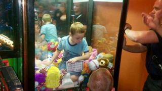 A young boy is stuck inside a stuffed toy machine, on top of the stuffed toys, with two fire officers trying to get him out, 8 February 2017
