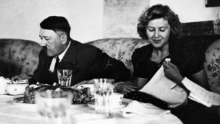 Hitler sentado em uma mesa comendo com uma mulher ao lado