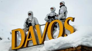 Armed security personnel stand guard on the rooftop of a hotel, next to letters reading "Davos"