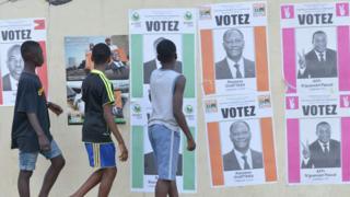 Boys walk past Ivory Coast's presidential election candidate campaign posters on October 14, 2015 in Cocody, Abidjan