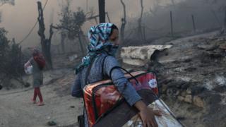 Refugee in mask with belongings under her arm after fire at Greek refugee camp following coronavirus outbreak