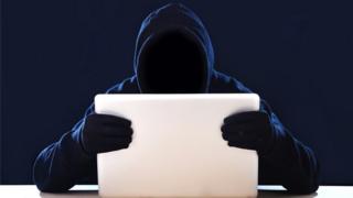 Imagen de hombre encapuchado mirando una computadora