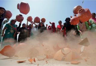 Women throw earthen pitchers onto the ground