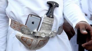 Un bailarín pone su iPhone de Apple junto a su tradicional daga omaní durante una ceremonia de bienvenida en Muscat, Omán (5 de noviembre de 2016).