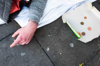 A homeless man next to a piece of cardboard with coins on