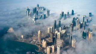 An aerial view of high-rise buildings emerging through fog covering the skyline of Doha, as the sun rises over the city, in Doha, Qatar, 15 February 2014