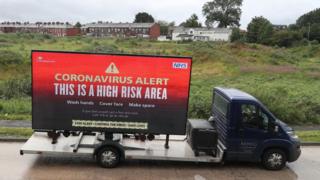 A lorry with a "Coronavirus Alert" sign on the back sits in front of a field in Oldham