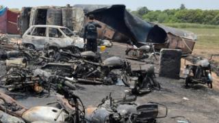 A member of an Anti Terrorist Squad (C) takes images of a burst and burnt out Oil tanker (R background) at the site of an accident on the outskirts of Bahawalpur, Pakistan, 25 June 2017.