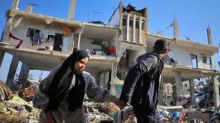 Palestinian people walk past a destroyed building in the Al-Maghazi refugee camp in central Gaza Strip, on 16 January 2024