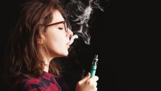 Молодая женщина в очках и курить электронную сигарету.