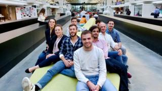 Funcionários da Advitam sorrindo e sentados em banco dentro de prédio corporativo