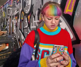 A young woman with dyed hair looks at her mobile phone