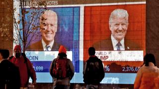 Trump / Biden on a screen with people watching on