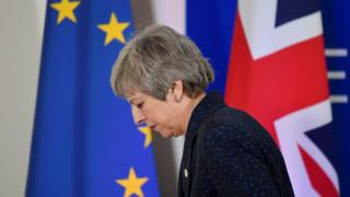 File photo: Theresa May looks down as she walks in front of an EU flag and a UK flag, 22 March 2019
