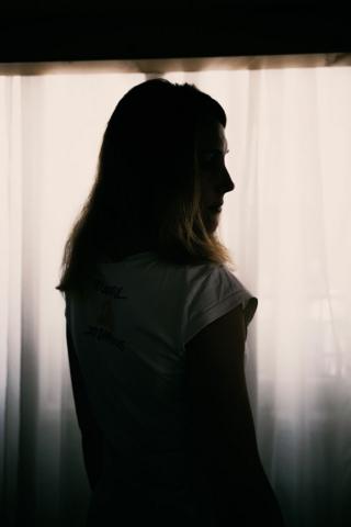 A woman stands next to window with the curtains pulled