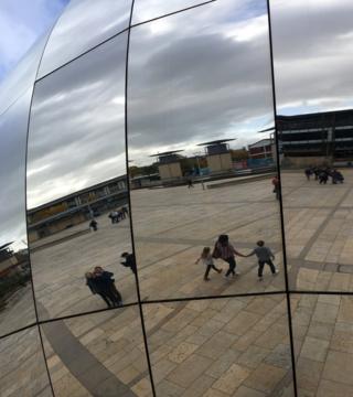 Reflections of people walking by a silver mirrored ball