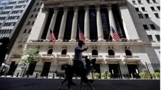 A man walks a dog in the shade away from the midday sun past the New York Stock Exchange (NYSE) building in Manhattan, during hot weather in New York City, New York, U.S., August 11, 2020