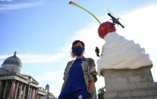 Artist Heather Phillipson stands in front of a sculpture depicting a whirl of cream with a cherry, fly and drone on top