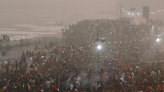 In the smog, a large crowd of Hindu worshippers entering the River Yamuna