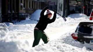 ニューヨークで雪に埋もれた車を書き出そうとする男性(24日)
