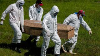   Los trabajadores del cementerio usan trajes protectores cuando realizan un funeral. 