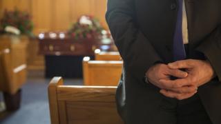 Man standing, coffin in background