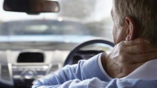 Driver holds his neck, apparently in pain, while sat at wheel of car