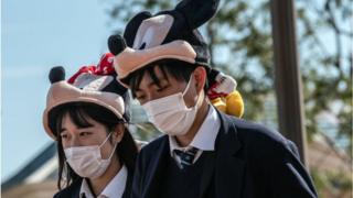 Students wearing Disney character hats and face masks leave Tokyo Disneyland, March 2020