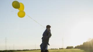 Мужчина с мальчиком на плечах держит воздушные шарики