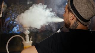 Hombre joven de espaldas fumando de una cachimba.