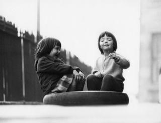 Two young girls playing in a tyre, 1966.