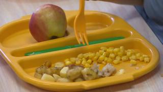 Школьную еду едят из желтого подноса с кукурузой, картофелем и яблоком на стороне