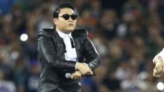 Співак Psy виконує рухи танцю Gangnam Style на сцені з двома танцюристами