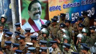 Члены Специальной оперативной группы Шри-Ланки и сотрудники полиции стоят рядом с плакатом недавно назначенного премьер-министра Махинды Раджапакса, 28 октября 2018 года