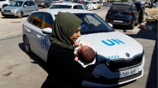 A woman carries her baby in front of a UN car at a United Nations centre in Khan Younis in the southern Gaza Strip on 13 October 2023.