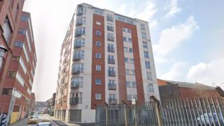 A modern block of flats sits at one corner of a junction. It is nine floors high.