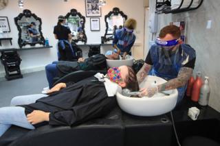 Customers wearing masks have their washed in basins in a hairdressers