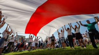 Belarusian people hold a giant historical flag of Belarus during a rally in support of the Belarusian opposition