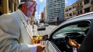 Minister Edilson Paes from the Basilica Cathedral wears a face shield as he gives communion in a drive-through ceremony during an Easter Sunday service during the coronavirus pandemic in Curitiba on 12 April 2020