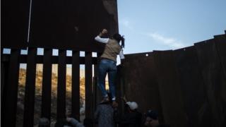 Central American migrants climb the metal barrier separating Mexico and the US on 2 December, 2018