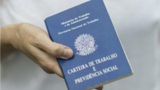 Imagem mostra homem segurando carteira de trabalho
