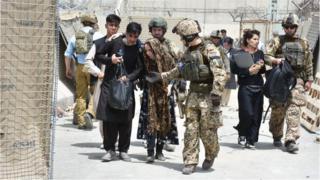 Soldiers help a women, fell due to high temperature at the Kabul International Airport as thousands of Afghans rush to flee the Afghan capital of Kabul,