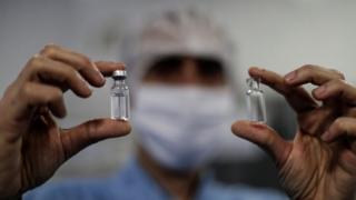 Homem segura frascos da vacina de Oxford
